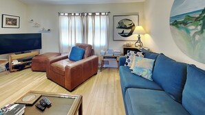 A living room with a brown leather sofa, a blue sofa, a TV, and a painting on the wall. - Sassy Seahorse | Pet Friendly + Near Area Fun! (Surf City)
