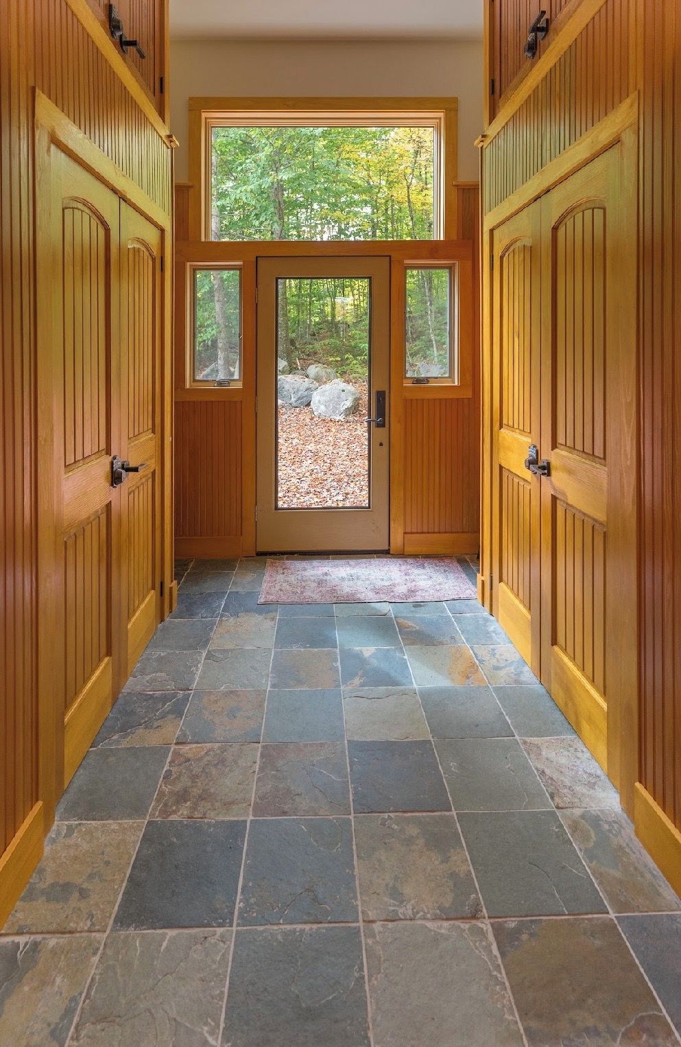 A wooden door with a view of a forest, leading to a stone-tiled floor.
