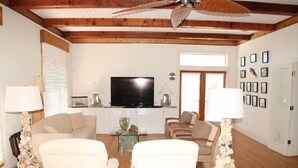 Ein Wohnzimmer mit Fernseher, zwei Sesseln, einem Couchtisch und einem Deckenventilator.