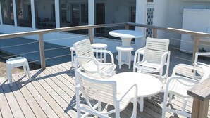 Eine überdachte Terrasse im Freien mit weißen Plastikmöbeln, darunter Stühle und ein Tisch, mit Blick auf einen Swimmingpool.
