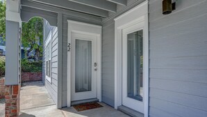 Una entrada de casa con una puerta blanca, una puerta de cristal y un muro de ladrillo.