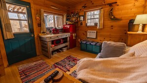 A cozy cabin interior with a wooden interior, a kitchenette, a sofa, and a window with curtains.