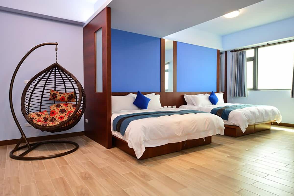 Habitación de hotel con dos camas, una silla colgante y un ventanal grande.