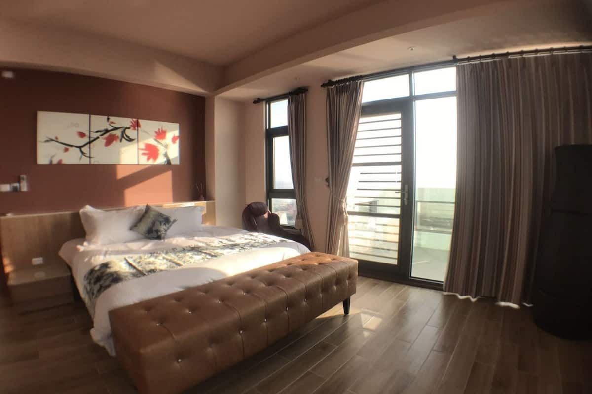 Un dormitorio amplio con una cama grande, una zona de estar y un balcón con cortinas.