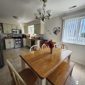 A kitchen with white cabinets, a dining table with chairs, a chandelier, and a window with blinds. - 5 Star AMAZING Perfect Beach Retreat just for you.  Cozy, Clean, Comfortable (Brigantine)