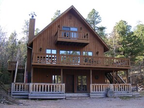 A wooden cabin with a balcony, a chimney, and a porch.