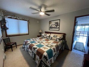 A bedroom with a bed, a chair, a ceiling fan, a window, and a door leading to a balcony.