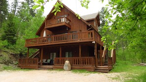 Une cabane en bois à deux étages, dotée d’un balcon, d’une véranda et d’une pierre à l’entrée.