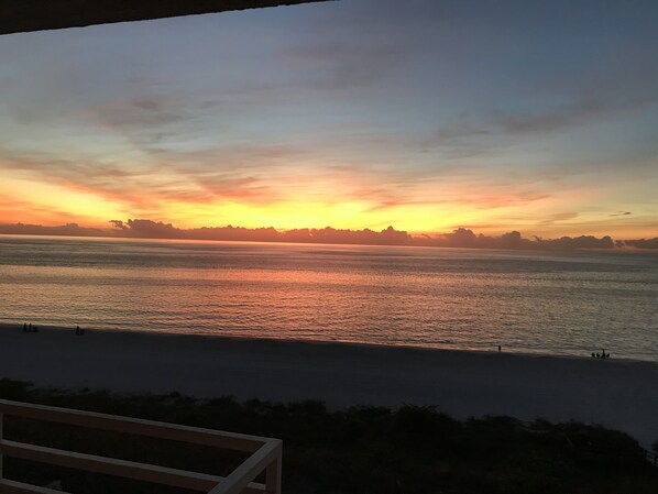 Um pôr do sol sobre águas calmas, com o contorno distante da costa.