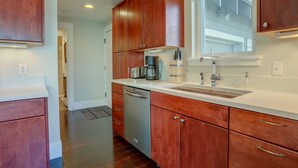 A modern kitchen with wooden cabinets, a dishwasher, a sink, and a window providing natural light. - Surfsup - Downtown, River View, A/C, Stay for a Month! Great Rates! (Hood River)