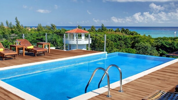 A swimming pool with a wooden deck, lounge chairs, and a view of the ocean. - Beach 1 Block, 2BR, Garage, Roof Pool, L3 (Playa del Carmen)