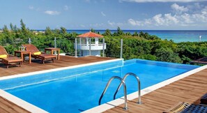 A swimming pool with a wooden deck, lounge chairs, and a view of the ocean.