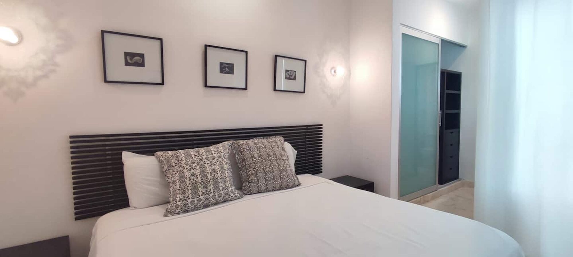 A bedroom with a bed, a headboard, and three framed pictures on the wall.