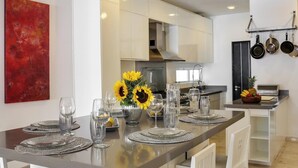 A modern kitchen with a central island, white cabinetry, and a red abstract painting on the wall. - Beach 1 Block, 2BR, Garage, Roof Pool, L3 (Playa del Carmen)