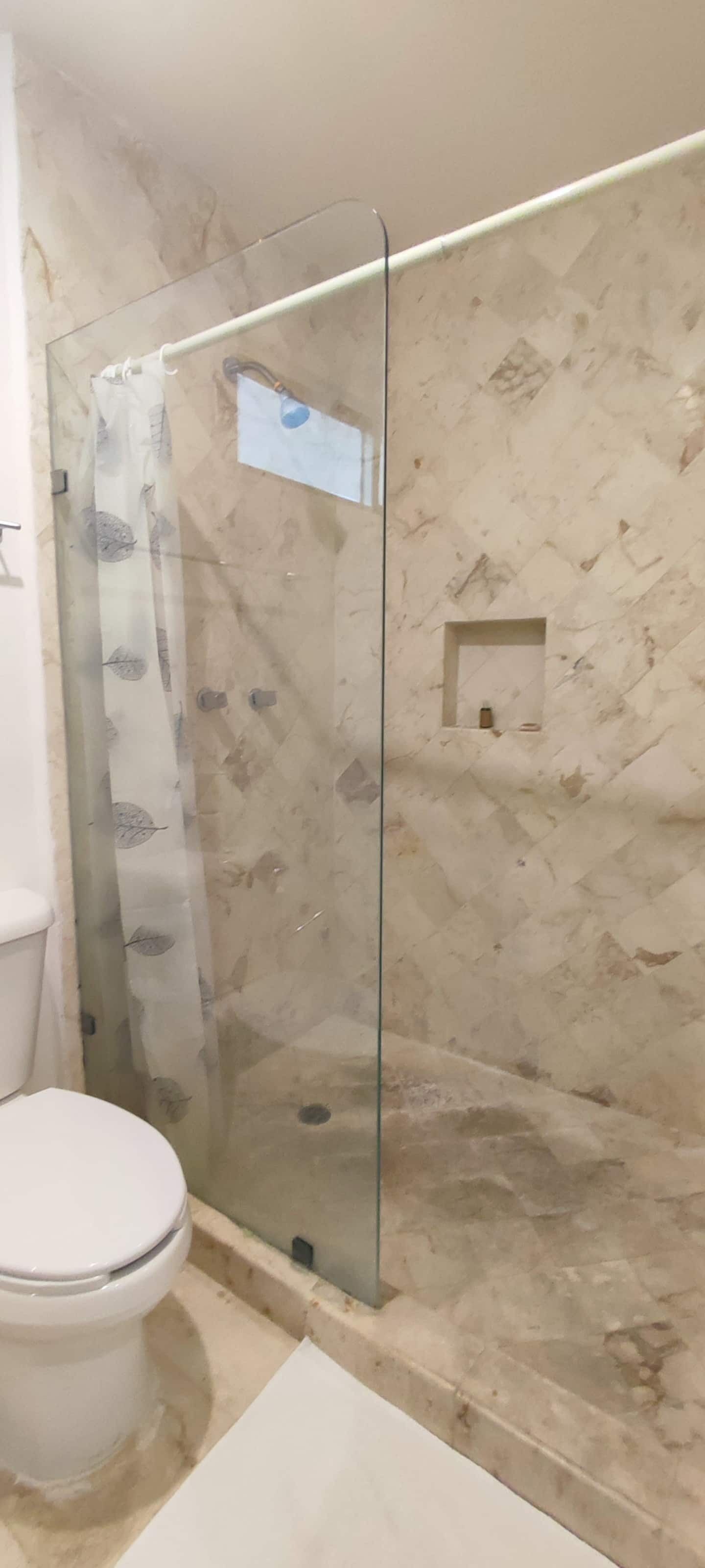 Une salle de bain avec une douche à parois de verre, des toilettes et un mur en marbre.