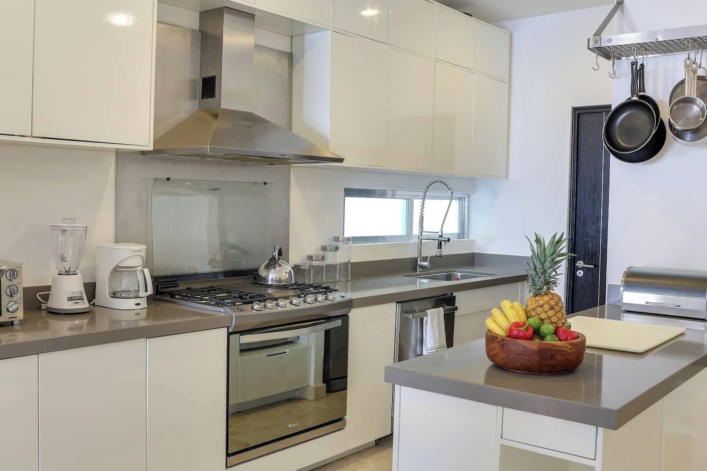 A modern kitchen with white cabinetry, a stainless steel range, a built-in oven, a coffee maker, and a fruit bowl on the counter.