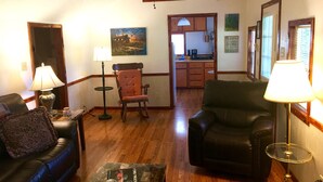 A living room with a wooden floor, a ceiling fan, a rocking chair, a leather sofa, and a coffee table with a book. - Cabin # 2, Kentucky Lake, Bass Fishing, Camden, Tn, (Nashville 1, Memphis 1.5) (Camden)