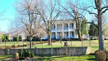 A large, two-story building with a symmetrical facade, surrounded by a well-maintained lawn and a stone wall.