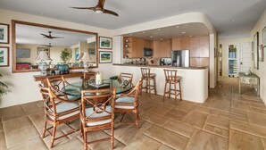 Una cocina moderna con armarios de madera, una isla central y una zona de comedor con sillas de mimbre y una mesa de vidrio.