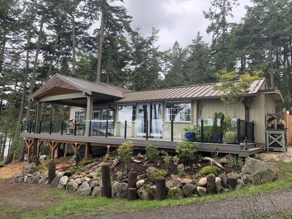 Una cabaña con terraza, rodeada de árboles y un jardín rocoso.