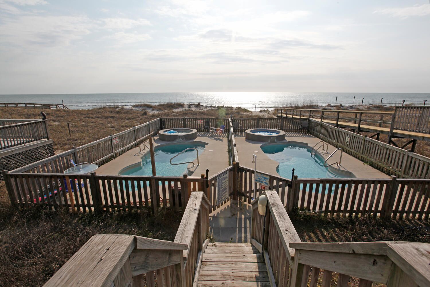 A pool area with two hot tubs and a wooden deck leading to the pool.