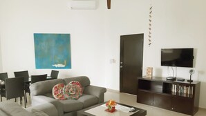 A modern living room with a grey sofa, a coffee table, a flat-screen TV, a bookshelf, and a painting on the wall. - 2BR, Central, Sleeps 6, Garage, Roof Pool, A306 (Playa del Carmen)