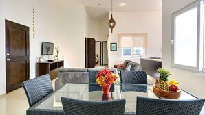 A modern living room with a glass-top dining table surrounded by wicker chairs, a sofa, and a coffee table with a floral centerpiece. - 2BR, Central, Sleeps 6, Garage, Roof Pool, A306 (Playa del Carmen)