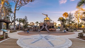 Un parque con un diseño de brújula grande, juegos infantiles y un paseo marítimo de madera.