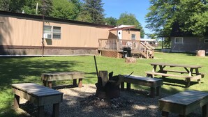 Ein Campingplatz mit Picknicktischen, einer Feuerstelle und einer Holzterrasse.