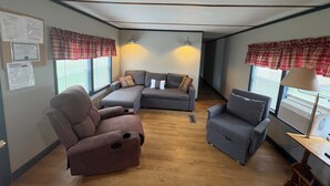 Ein möbliertes Wohnzimmer mit Ecksofa, zwei Sesseln, einem kleinen Tisch und einer Lampe.