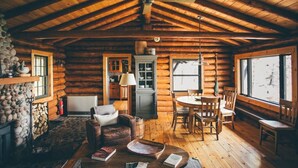 Interior de una cabaña de troncos con comedor, chimenea y ventanas amplias.