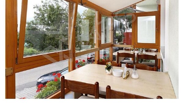 A dining area with a wooden table and chairs, large windows, and a view of the street. - Hotel Rajsky (Cesky Krumlov)