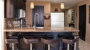 Une cuisine moderne avec des meubles de couleur sombre, un plan de travail en granit, un réfrigérateur en acier inoxydable et un coin bar avec des tabourets.
