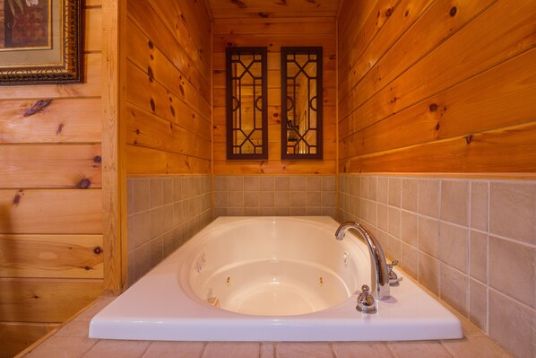 Un baño de cabaña de madera con una bañera grande, paredes de madera y una zona de ducha con azulejos.