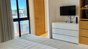 Een slaapkamer met een bed, een televisie, een houten kledingkast en een glazen schuifdeur naar een balkon.