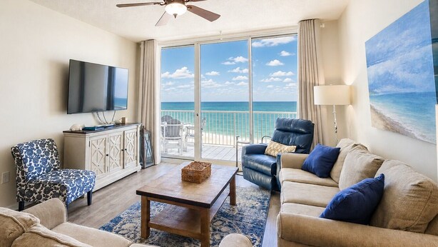 A living room with a TV, a sofa, a chair, a coffee table, and a view of the ocean.