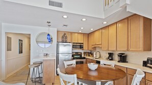 A modern kitchen with wooden cabinets, a stainless steel refrigerator, and a round dining table with white chairs. - 44- Gorgeous BEACH FRONT Condo with Loft in Crystal Beach. Coral Reef Club (Destin)