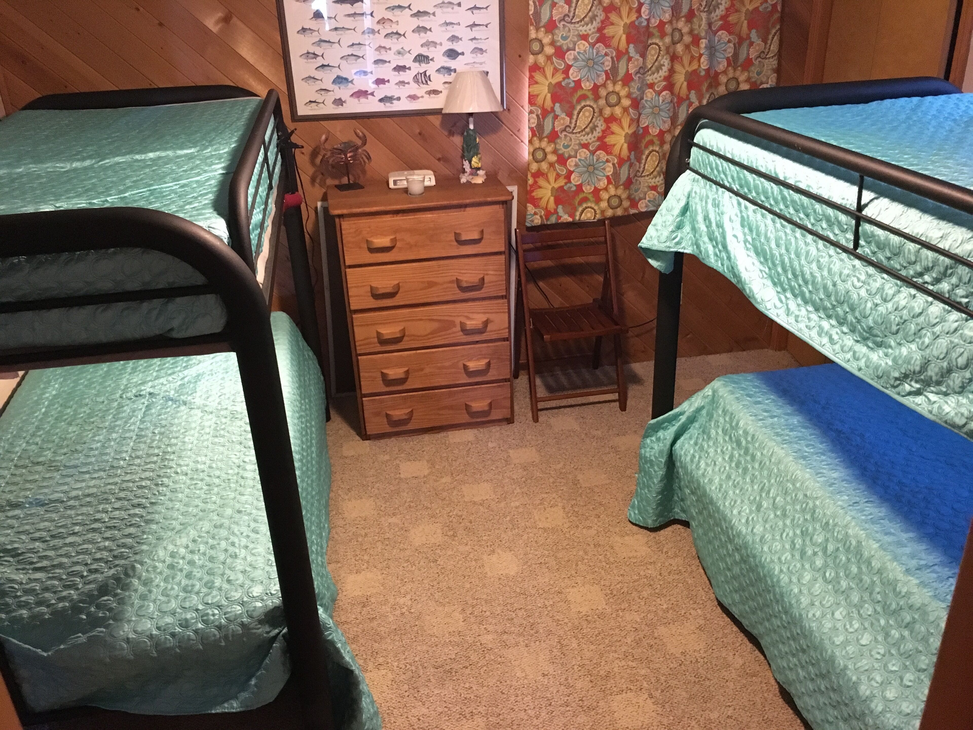 Une chambre avec des lits superposés, une commode en bois, une chaise et un mur orné d’une affiche de poissons.