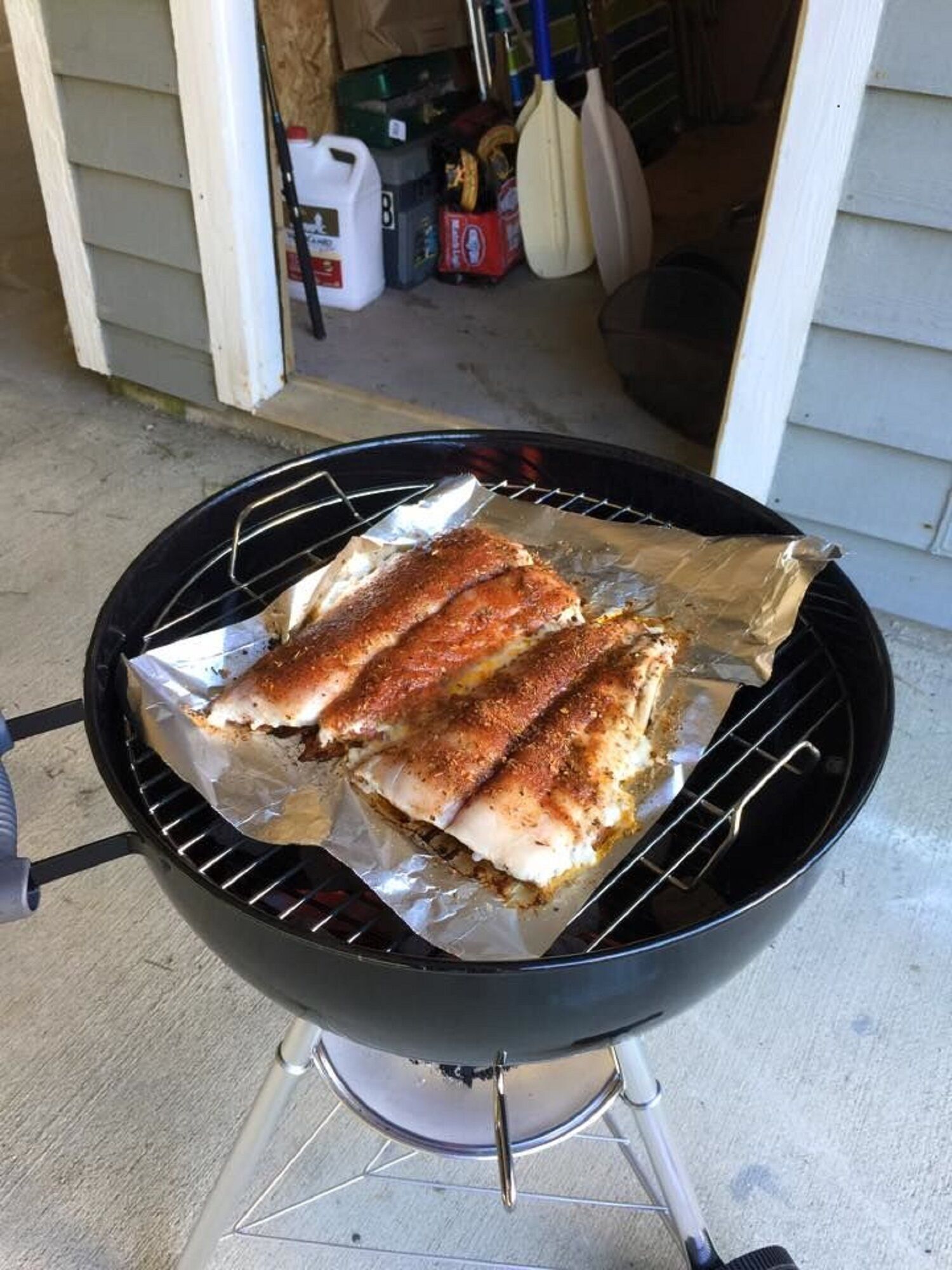 A charcoal grill with foil-wrapped food on a concrete surface.