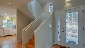 A modern kitchen with white cabinets and a wooden floor, a staircase with white railings, and a door with a view of the outdoors. - Fir Mountain Escape - Stunning Views, River & Mountain Views, Hot Tub (Hood River)