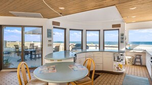 A modern kitchen with large windows, a dining area with a round table, and a view of the beach. - Stunning Oceanfront Home on Quiet Lane with Bay and Ocean Views. Hot tub! (Beach Haven)