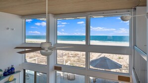 A room with large windows overlooking a beach, a ceiling fan, and a view of the ocean. - Stunning Oceanfront Home on Quiet Lane with Bay and Ocean Views. Hot tub! (Beach Haven)