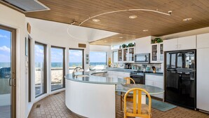 A modern kitchen with a curved island, large windows, and a view of the beach. - Stunning Oceanfront Home on Quiet Lane with Bay and Ocean Views. Hot tub! (Beach Haven)