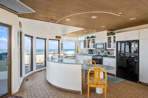 Enjoy ocean views from the kitchen's multiple windows, featuring a curved island with a glass top and stainless steel appliances.