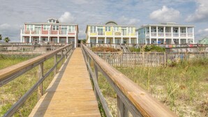 A wooden boardwalk leading to colorful beach houses with multiple stories and balconies.