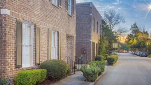Un bâtiment en briques de deux étages, avec des volets blancs, un trottoir et une rangée de voitures garées.