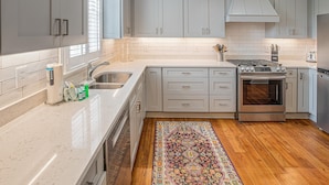 Une cuisine avec des meubles de couleur gris clair, un plan de travail blanc, un plancher en bois et un tapis à motifs.