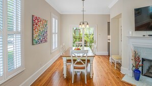 Un coin repas avec une table et des chaises en bois, une œuvre d’art colorée accrochée au mur et une cheminée surmontée d’un téléviseur.
