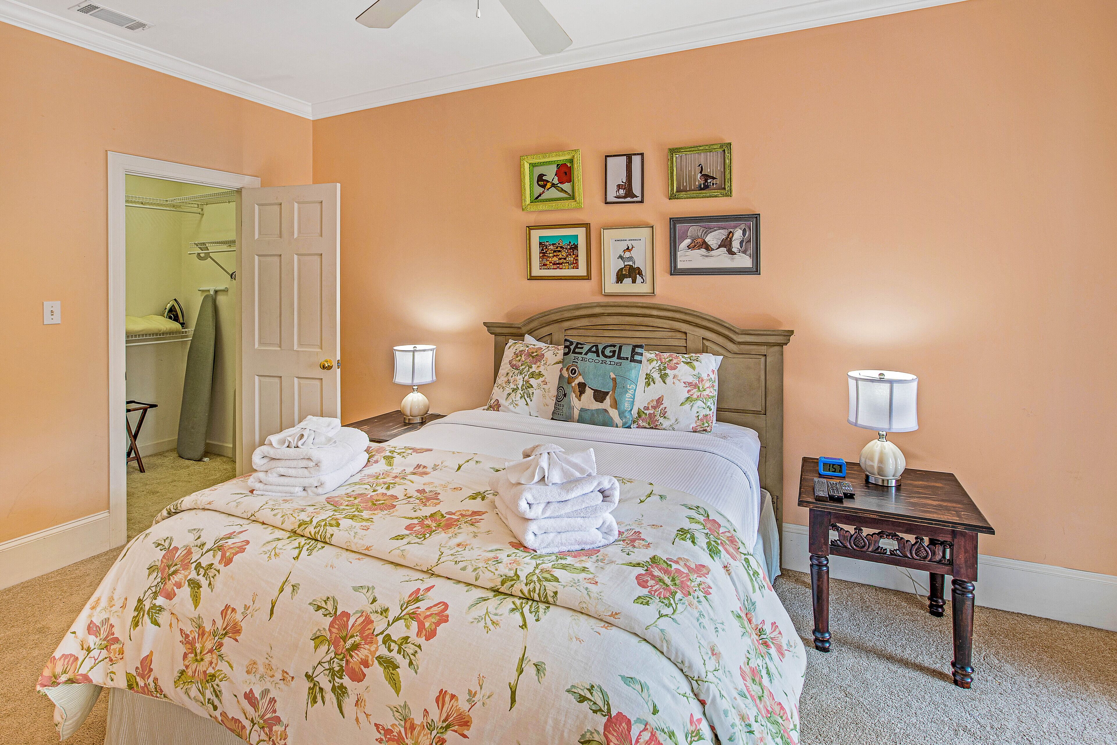 A bedroom with a bed, two bedside tables, a nightstand, a door, and a wall with framed pictures.