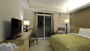 A hotel room with a bed, a desk with a TV, a chair, a lamp, and a view of the outside through a sliding door. - Hoya Resort Hotel Chiayi (Minxiong)